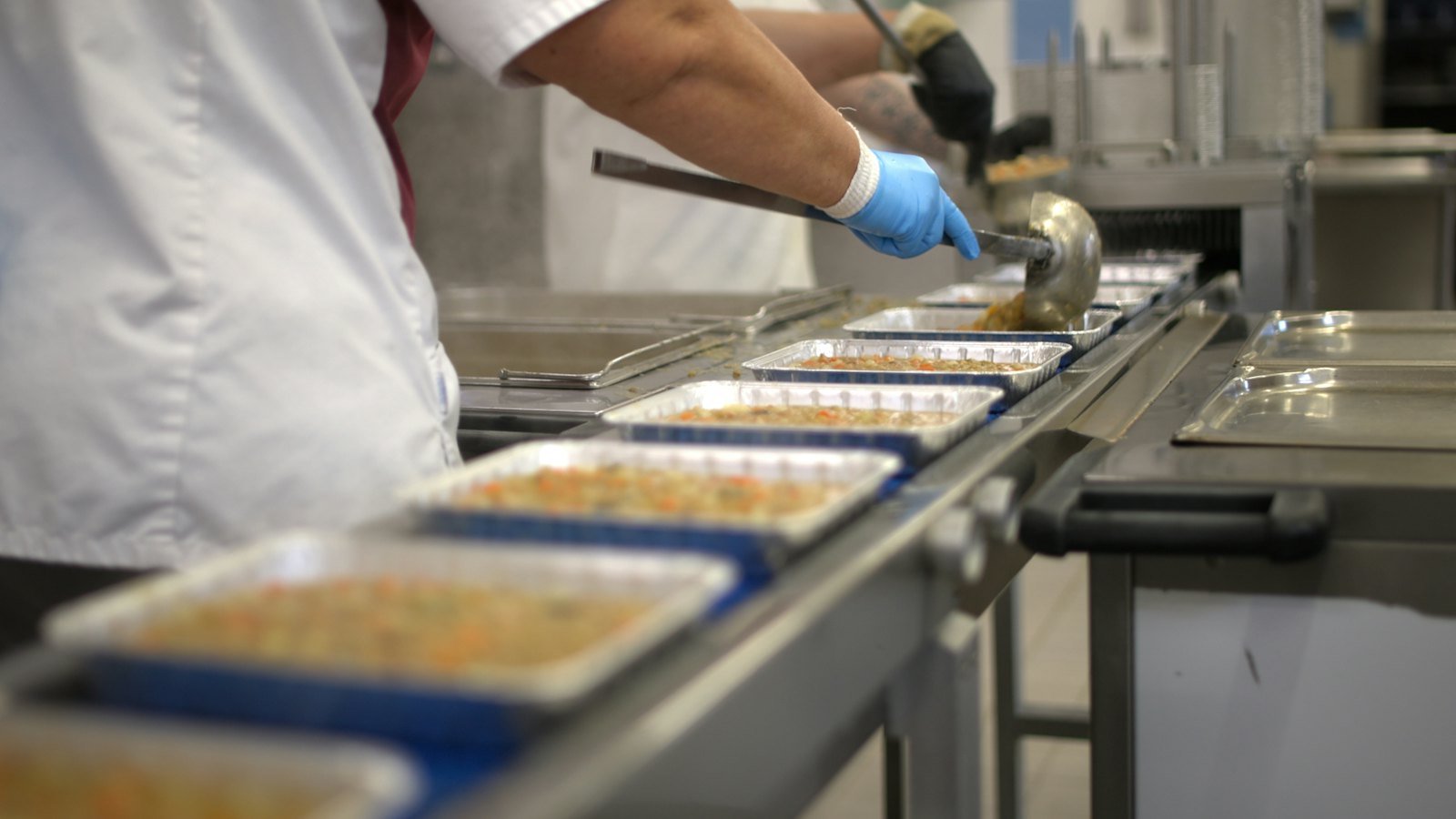 Gloved worker filling food trays on a conveyor